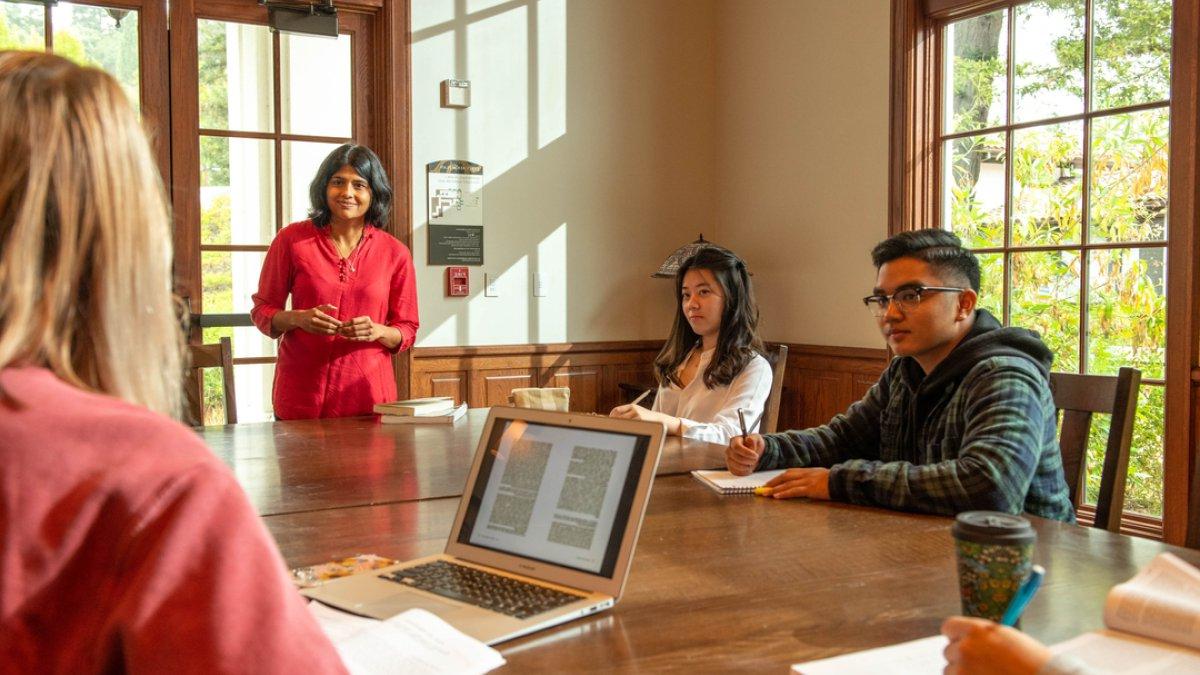 Two students and a professor discuss a text during class